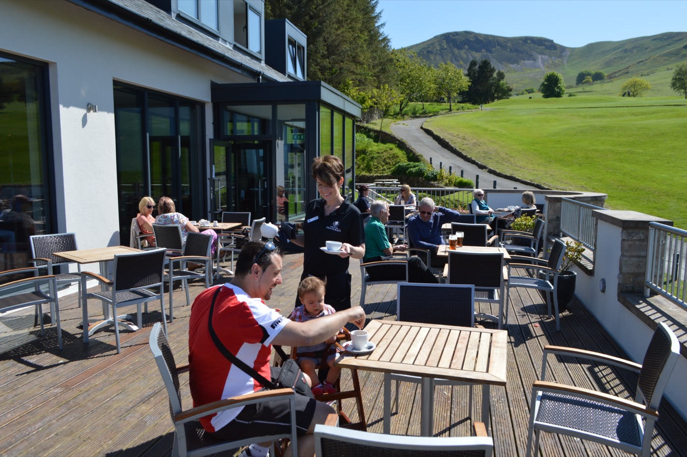 Diners on the sunny Brasserie balcony with Caerketton Hill behind
